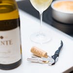 A glass of white wine beside a bottle and corkscrew on a table, ideal for wine lovers.