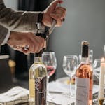A sommelier opening a wine bottle in a cozy indoor setting with wine glasses and candlelight.